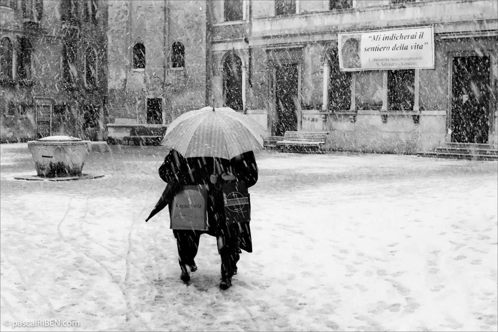 Two women are walking under an umbrella against the snow on Campo San Silvestro, Venice, Italy