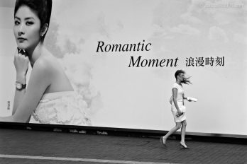 Hong Kong, China, June 16, 2010 - An occidental woman is walking in the wind in front of the giant photo of a Chinese woman