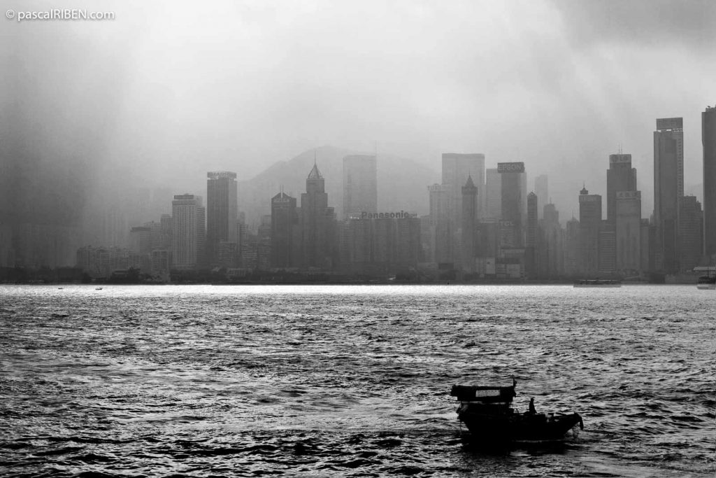 Small boat in Hong Kong harbor with Victoria Skyline in the background, seen from Avenue of Stars, on an early morning