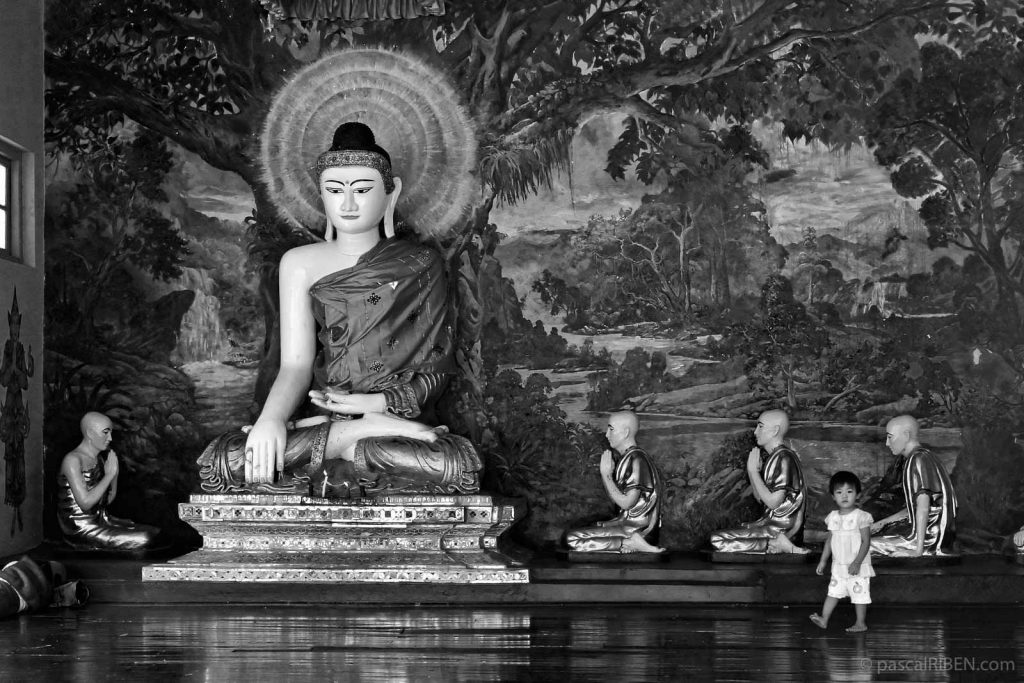 A little girl is walking inside a temple room with statues of Buddha and prayers.